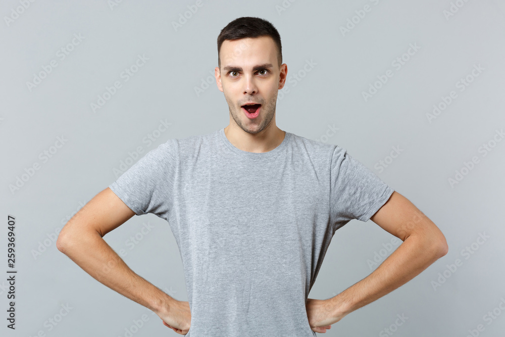 Portrait of bewildered amazed young man in casual clothes standing with arms akimbo on waist isolated on grey wall background in studio. People sincere emotions, lifestyle concept. Mock up copy space. Portrait of bewildered amazed young man in casual clothes standing with arms akimbo on waist isolated on grey wall background in studio. People sincere emotions, lifestyle concept. Mock up copy space.