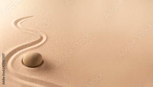 Spa wellness background of a zen meditation garden with sand and round stone. A nice curved line on sandy texture. Lots of copy space.