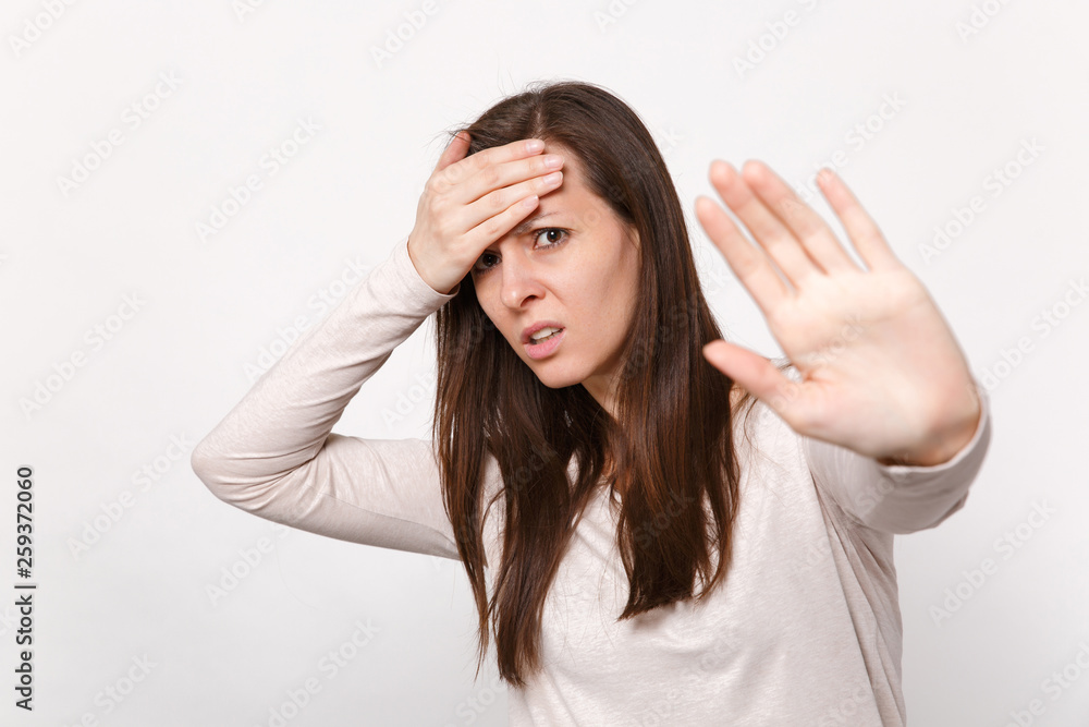 Tired young woman in light clothes putting hand on forehead, showing stop gesture with palm isolated on white wall background in studio. People sincere emotions, lifestyle concept. Mock up copy space. Tired young woman in light clothes putting hand on forehead, showing stop gesture with palm isolated on white wall background in studio. People sincere emotions, lifestyle concept. Mock up copy space.