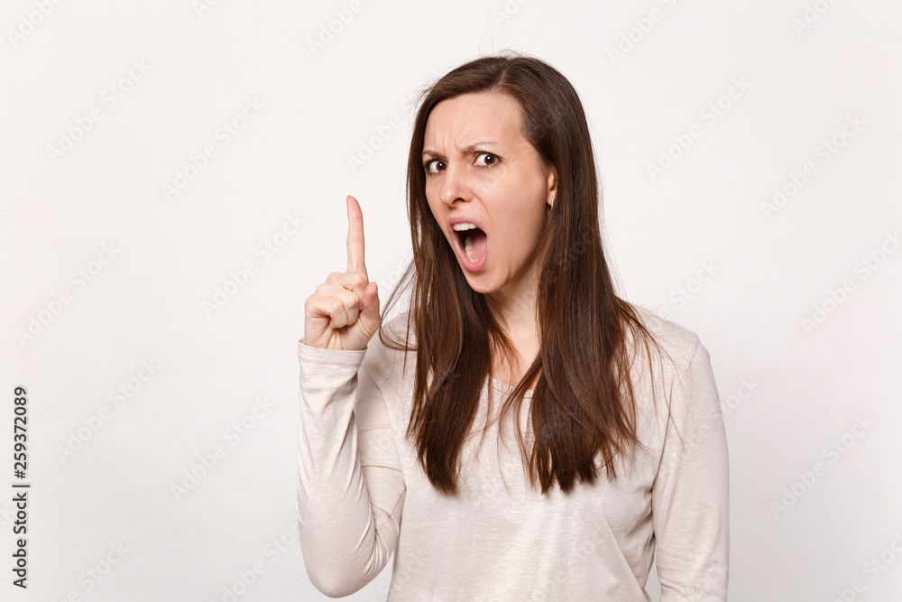 Angry strict young woman in light clothes screaming and swearing, pointing index finger up isolated on white wall background in studio. People sincere emotions, lifestyle concept. Mock up copy space. Angry strict young woman in light clothes screaming and swearing, pointing index finger up isolated on white wall background in studio. People sincere emotions, lifestyle concept. Mock up copy space.