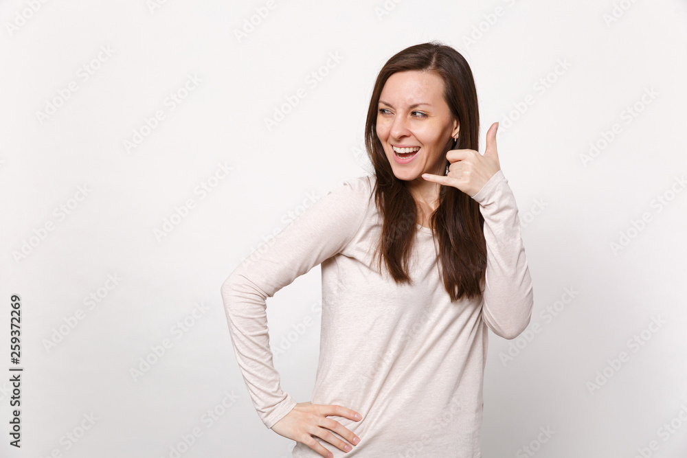 Cheerful young woman in light clothes looking aside, doing phone gesture like says call me back isolated on white background in studio. People sincere emotions, lifestyle concept. Mock up copy space. Cheerful young woman in light clothes looking aside, doing phone gesture like says call me back isolated on white background in studio. People sincere emotions, lifestyle concept. Mock up copy space.