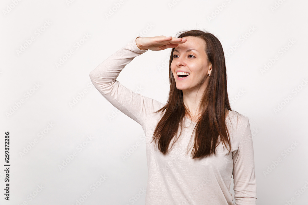 Portrait of smiling young woman in light clothes holding hand at forehead looking far away distance isolated on white wall background. People sincere emotions, lifestyle concept. Mock up copy space.
