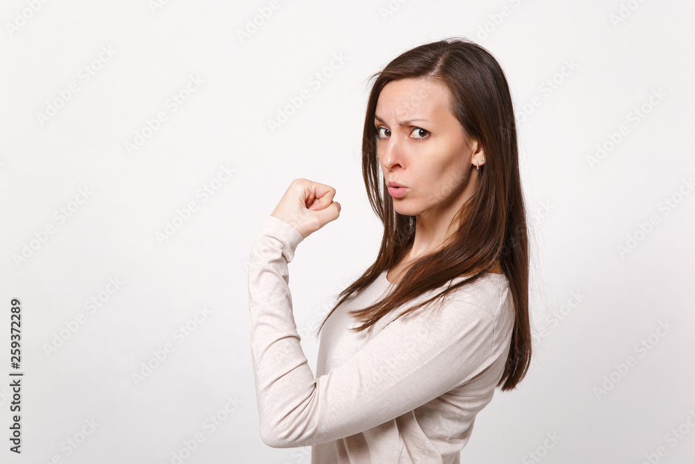 Portrait of strong serious attractive young woman in light clothes showing biceps, muscles isolated on white wall background in studio. People sincere emotions, lifestyle concept. Mock up copy space. Portrait of strong serious attractive young woman in light clothes showing biceps, muscles isolated on white wall background in studio. People sincere emotions, lifestyle concept. Mock up copy space.
