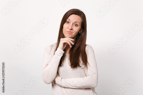 Portrait of puzzled young woman in light clothes looking camera, put hand prop up on chin isolated on white wall background in studio. People sincere emotions, lifestyle concept. Mock up copy space.