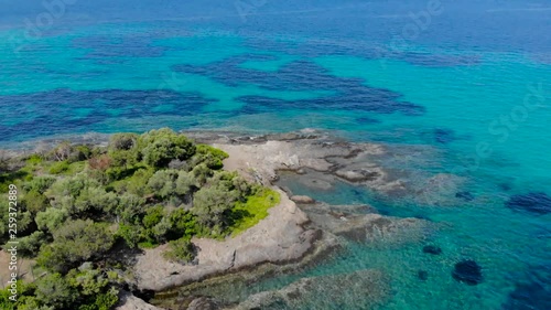 Aerial view of blue sea surface on rocky coast with light reflections. Top view of transparent turquoise ocean water surface and rocks on shore.