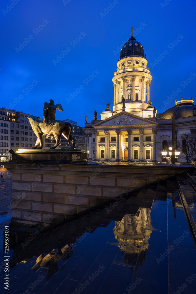 Lit Neue Kirche (Deutscher Dom, German Church or German Cathedral) and a statue in front of the Konzerthaus Berlin (Berlin Concert Hall) at the Gendarmenmarkt Square in Berlin, Germany, at dusk.