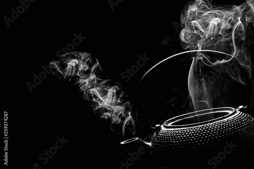 Antique teapot with steaming hot tea on black background.
