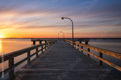 Warm golden light on an empty fishing pier at sunset. Soft pastel clouds streaking across the sky.