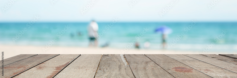 empty wood table on blurred of people walk on the beach with sunrise, warm tone