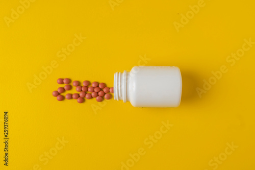 medical pills scattered from a white tube on a yellow background
