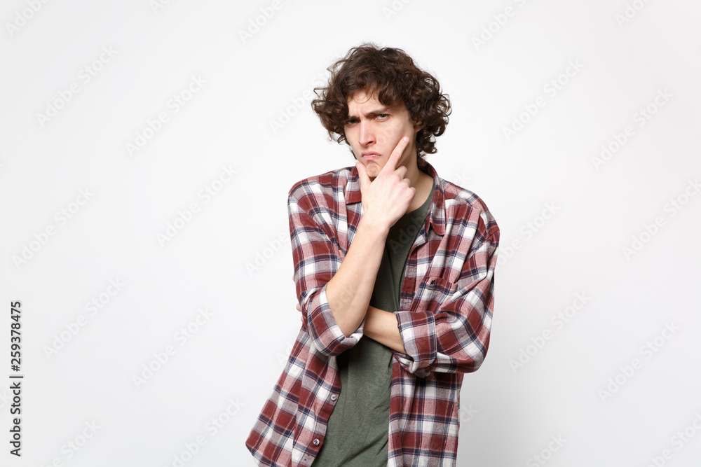 Portrait of suspecting pensive young man in casual clothes looking camera, put hand prop up on chin isolated on white wall background. People sincere emotions, lifestyle concept. Mock up copy space. Portrait of suspecting pensive young man in casual clothes looking camera, put hand prop up on chin isolated on white wall background. People sincere emotions, lifestyle concept. Mock up copy space.