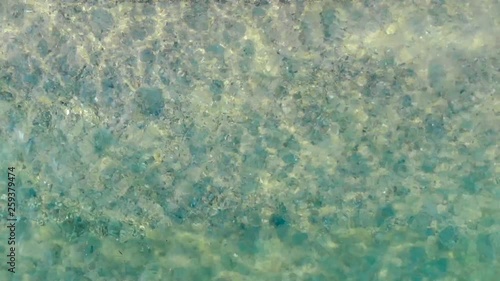 Aerial view of blue sea surface on sand beach with light reflections. Top view of transparent turquoise ocean water surface.