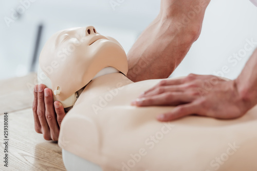 partial view of man holding dummy while practicing cpr during first aid training