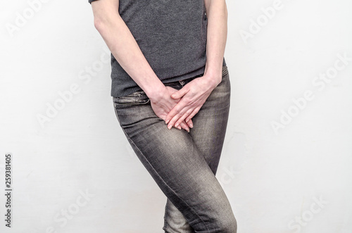 Young slim girl in jeans holds hands pressed between her legs. Women's health, gynecology.
