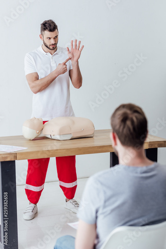 selective focus of handsome instructor pointing with finger during first aid training class photo