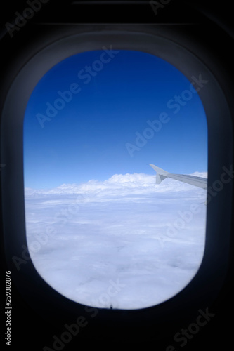 Airplane window with wing of an airplane flying above the clouds. People looks at the sky from the window of the plane.