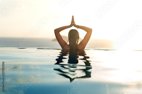 girl in the pool at sunset doing yoga with a view of the mountains and the sea