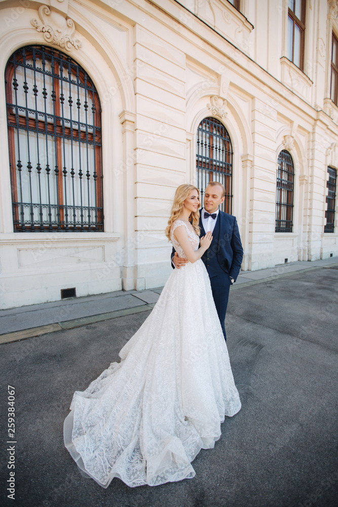 Couple walk near the big palace. Elegant groom and bride in their wedding clothes. Love