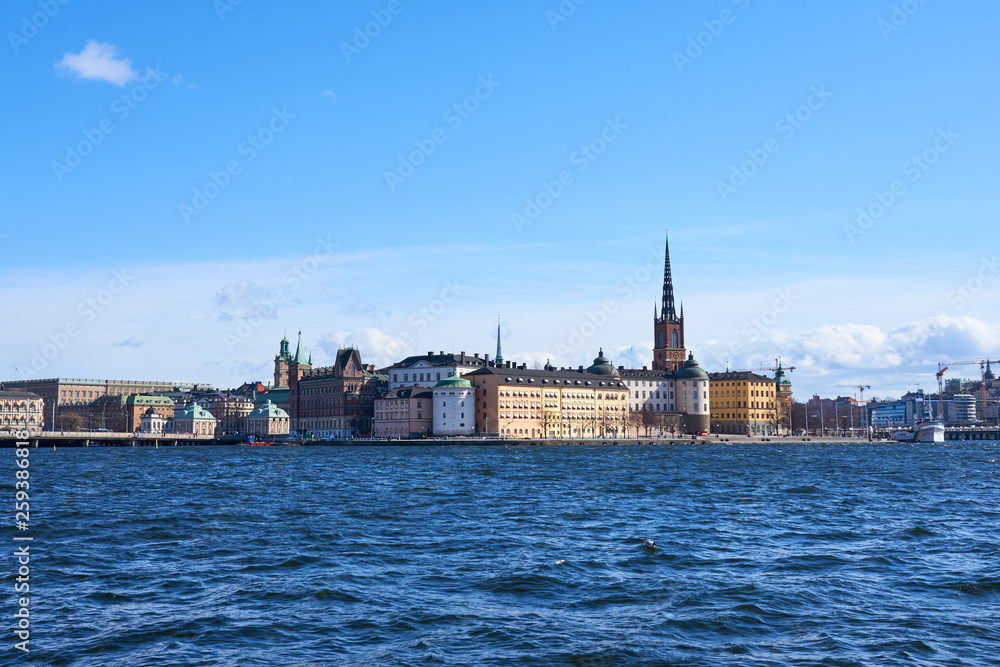 Old city of Stockholm with waves on blue water under the blue cloudy sky in sunshine.