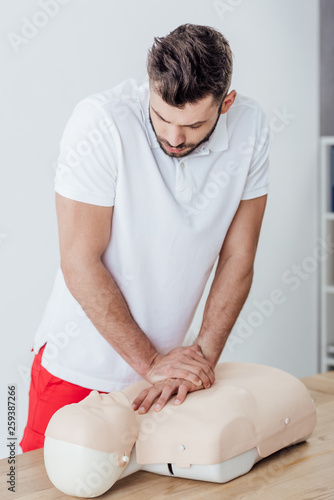 handsome man using chest compression technique on dummy during cpr training