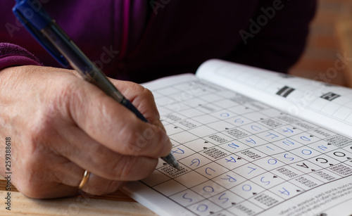 Hand of senior person doing crosswords puzzle's in a notebook. Leisure and free time.