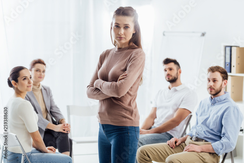 woman with arms crossed looking at camera while people sitting on chairs during group therapy session © LIGHTFIELD STUDIOS
