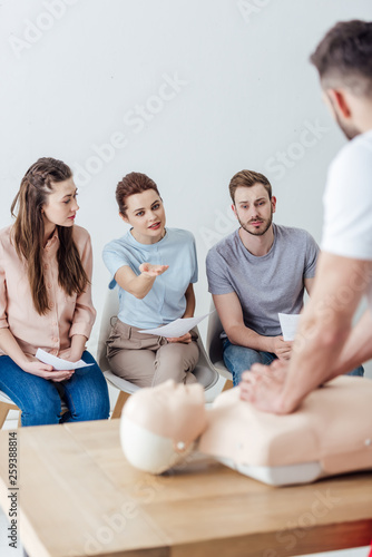 instructor performing chest compression on dummy during cpr training class with group of people photo