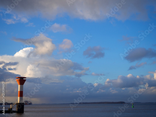 Leuchtturm an der Elbe mit vielen Wolken über strahelend blauem Himmel und grüner Boje photo