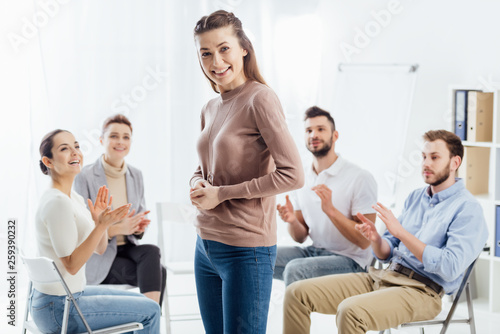 smiling woman looking at camera while people sitting and applauding during group therapy session © LIGHTFIELD STUDIOS
