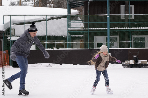Daddy and daughter skate on the rink under the open sky on a winter day