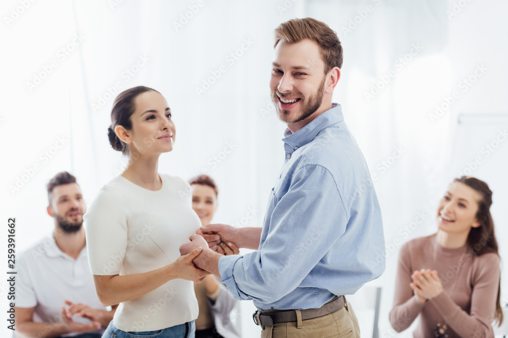 Fototapeta premium smiling man looking at camera and holding hands with woman during group therapy session