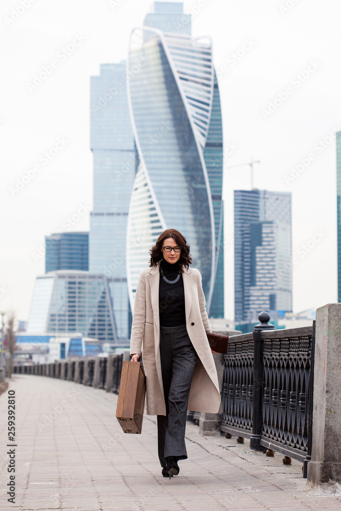 Beautiful business woman in a long light coat comes with a case in his hand on the waterfront