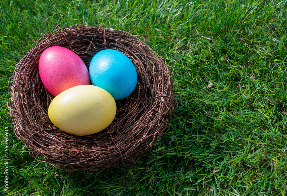 Three painted easter eggs in a nest on green grass