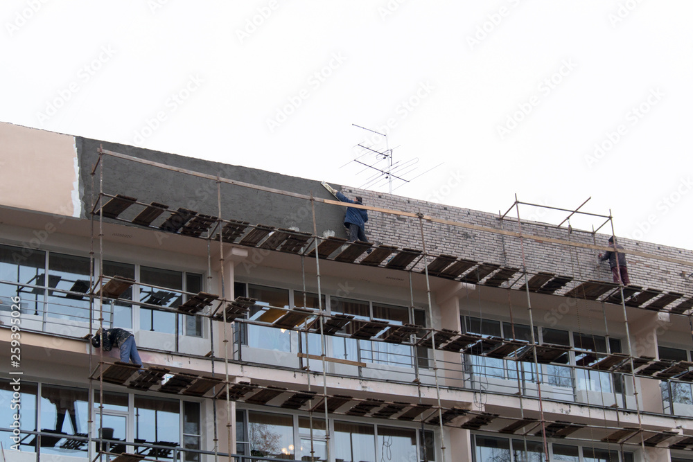View of the building with scaffolding. Workers repair the facade. View of the building with scaffolding. Workers repair the facade.