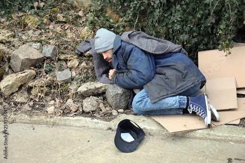 Poor homeless man lying on street in city