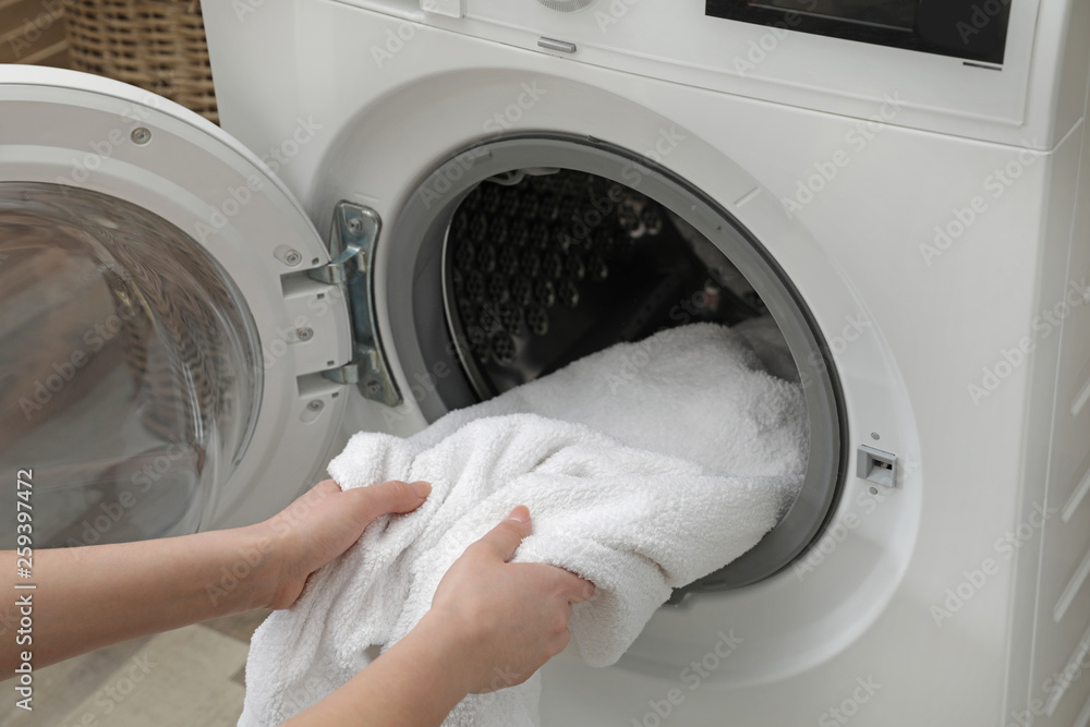 Woman taking clean towel from washing machine in laundry room, closeup Woman taking clean towel from washing machine in laundry room, closeup