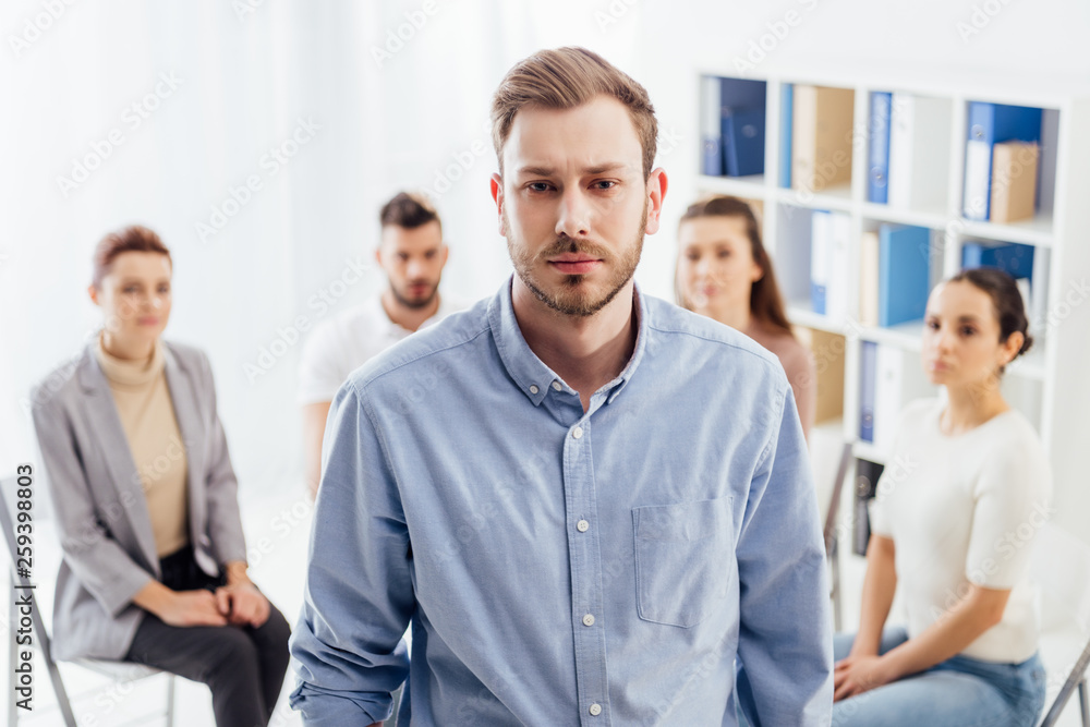 man looking at camera while people sitting during group therapy session