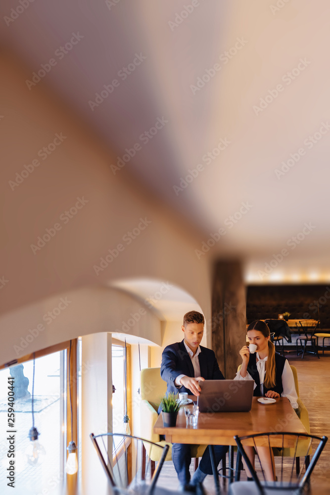 Obraz premium A stylish couple drinks morning coffee at the cafe and works with a laptop, young businessmen and freelancers