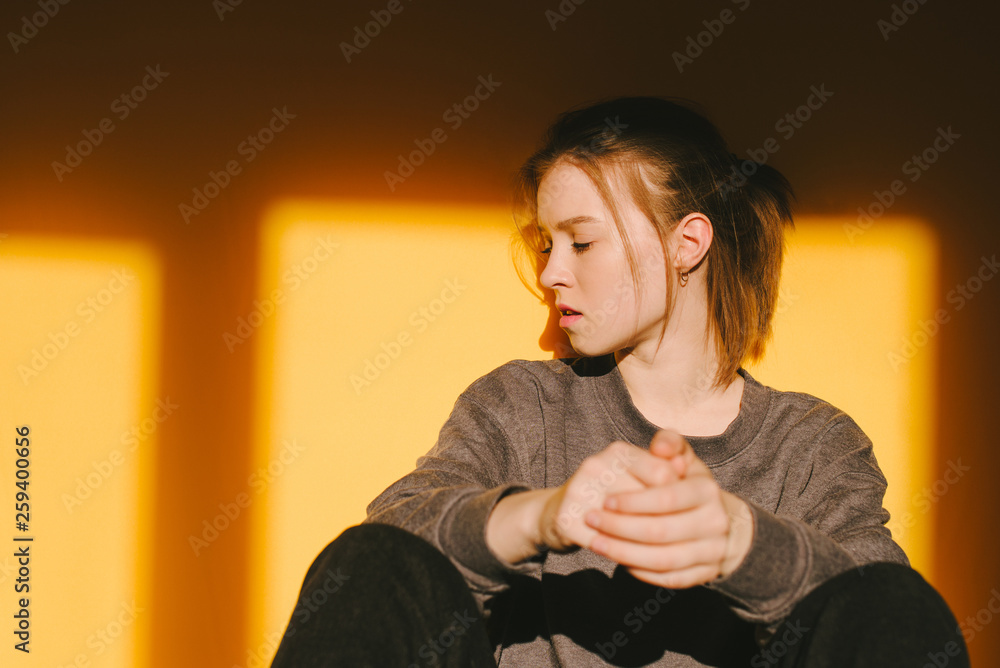 Close-up portrait of an attractive girl in casual clothing poses on the orange background in a home studio, sunshine. Woman poses on a yellow background, light from the window. Close-up portrait of an attractive girl in casual clothing poses on the orange background in a home studio, sunshine. Woman poses on a yellow background, light from the window.