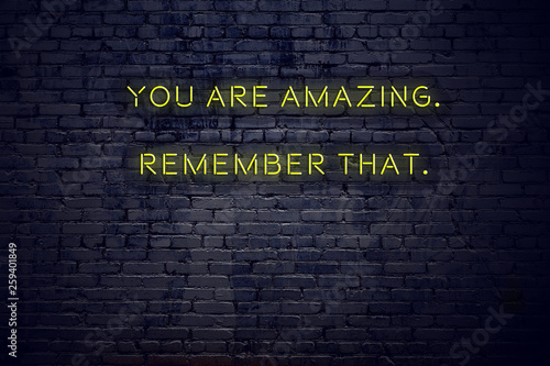 Positive inspiring quote on neon sign against brick wall you are amazing remember that