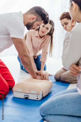 selective focus of instructor performing cpr on dummy during first aid training with group of people