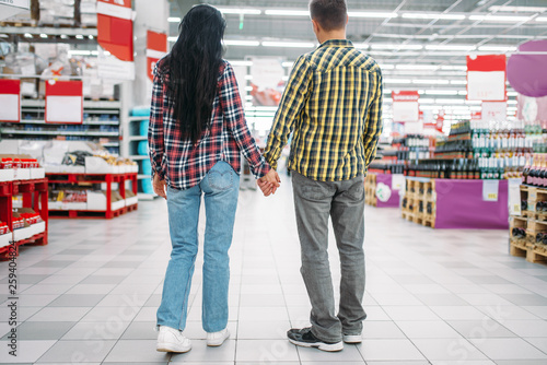 Young couple hold hands in supermarket, back view