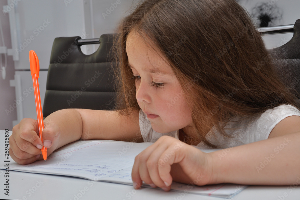 Portrait of cute caucasian girl doing homework at home . She learning to write with pen .She writes letters in notebooks. Portrait of cute caucasian girl doing homework at home . She learning to write with pen .She writes letters in notebooks.