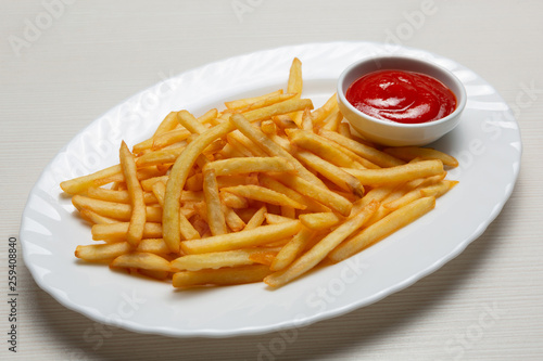 on a white plate, golden french fries, cut into strips, next to red sauce or ketchup in a bowl
