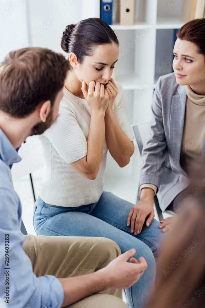 selective focus of worried woman covering mouth with hands during group therapy session selective focus of worried woman covering mouth with hands during group therapy session