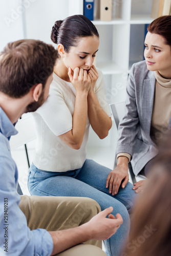 selective focus of worried woman covering mouth with hands during group therapy session