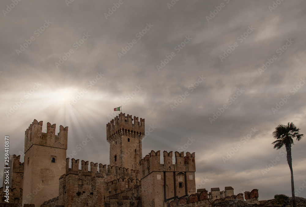 The Scaligero Castle (13th century) with a dramatic cloudy sky background, a rare example of medieval port fortification, Sirmione, Lake Garda, Lombardy, Italy