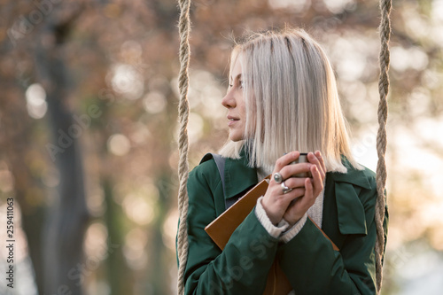 Young woman with bleached hair holding coffee cup while sitting on swing photo