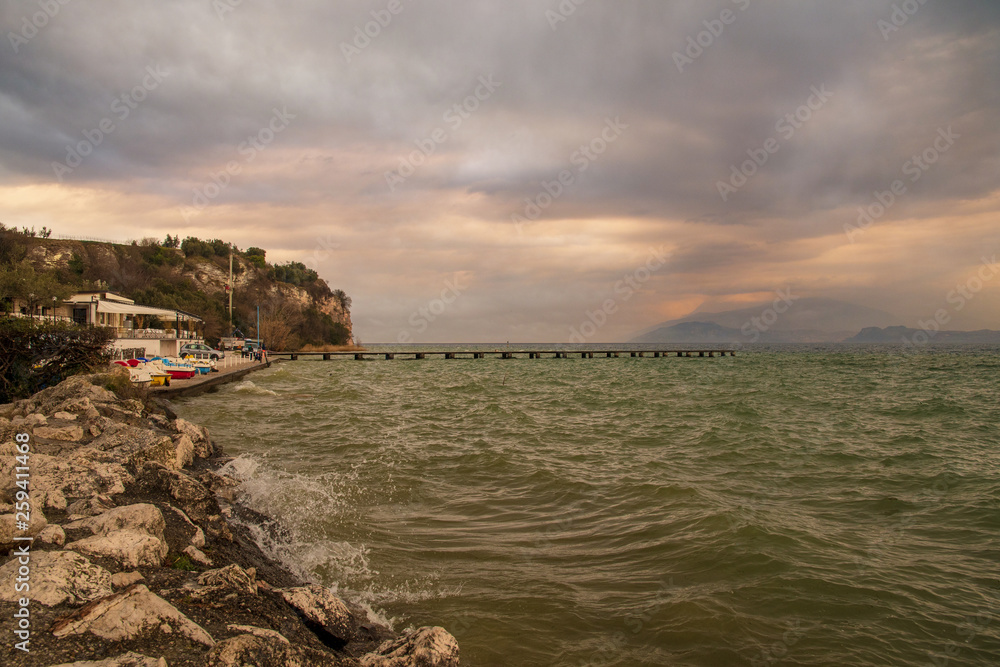 Scenic view of Lake Garda at sunset with a pier and a cliff in the background, Sirmione, Lombardy, Italy