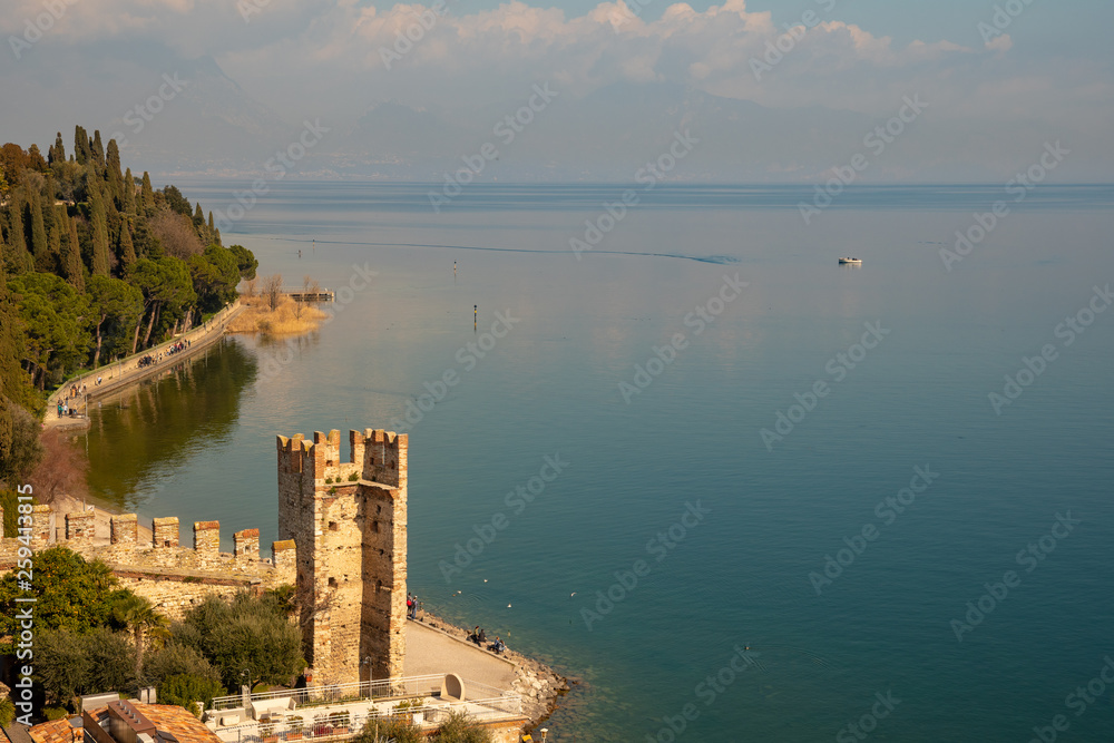 High angle view of the lake shore of Sirmione with the ruins of the medieval town walls with an angular tower (13th century), Lake Garda, Lombardy, Italy